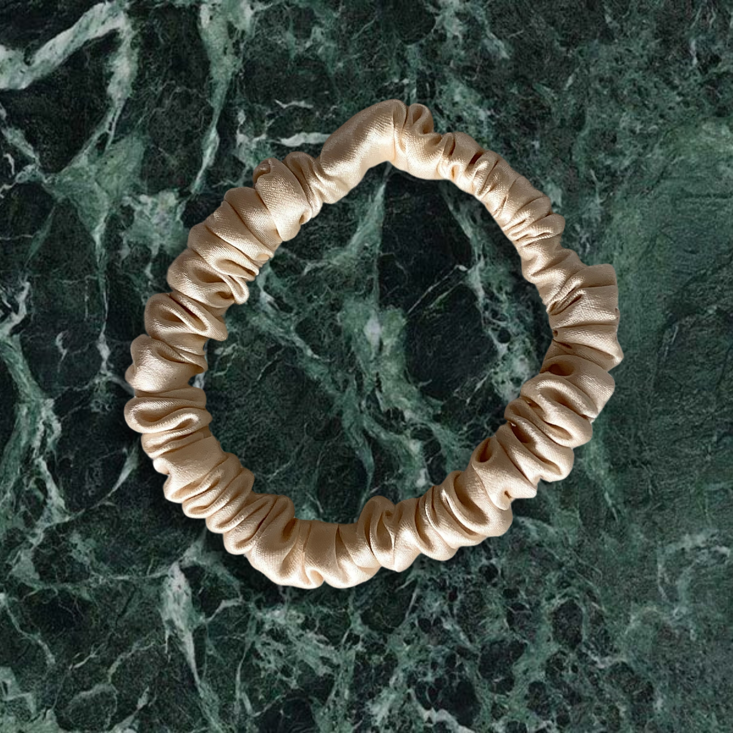 Champagne thin scrunchie on a green marble background.