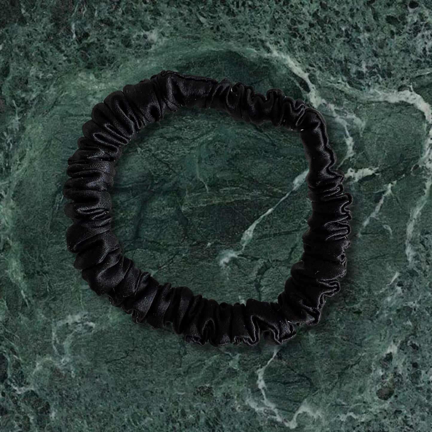 Black thin scrunchie on a green marble background.