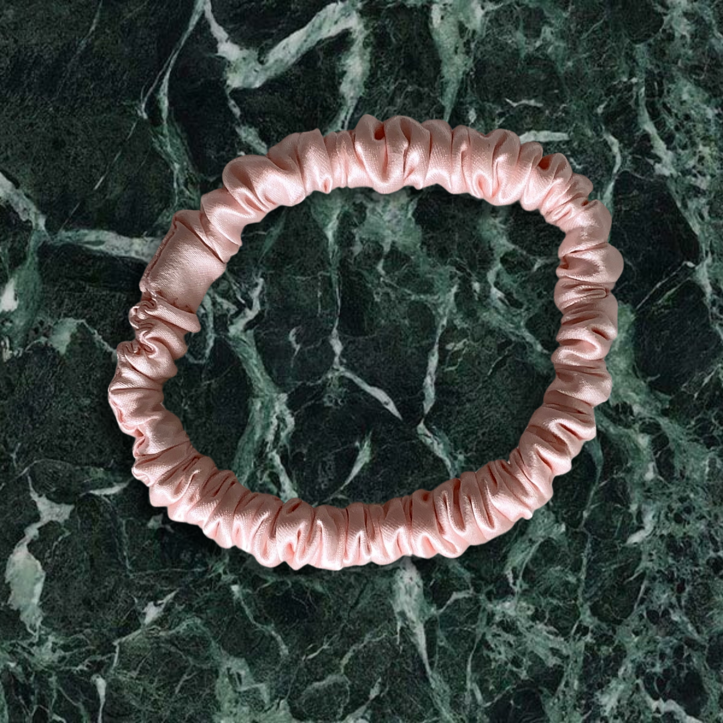 Pink thin scrunchie on a green marble background.